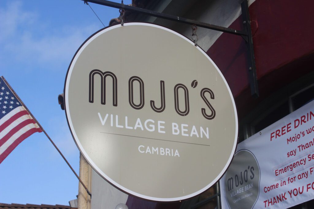 A charming sign for Mojo's Village Bean attached to a building, drawing attention to the local coffee spot.