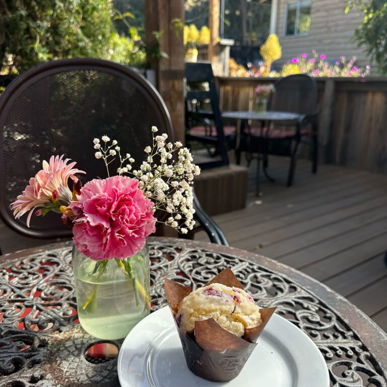 A patio table with fresh flowers and muffin.