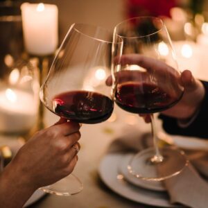 Cheers. Couple in love drinking wine. Romantic date by candlelight at night. Hands man and woman hold glasses at home. Toast. Dinner setup table for couple on Valentine's day. Proposal hand and heart.