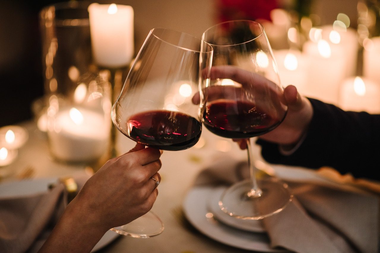 Cheers. Couple in love drinking wine. Romantic date by candlelight at night. Hands man and woman hold glasses at home. Toast. Dinner setup table for couple on Valentine's day. Proposal hand and heart.
